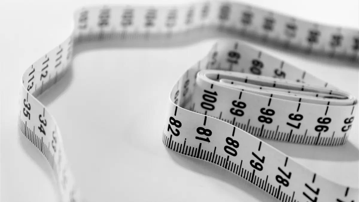 A flexible measuring tape coiled on a flat surface, showing various measurement markings.
