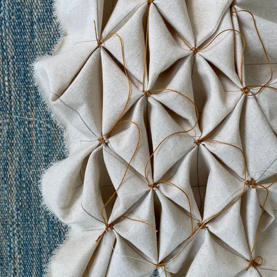 Textile surface featuring intricate fabric manipulation with pleats, knots, and structured folds.