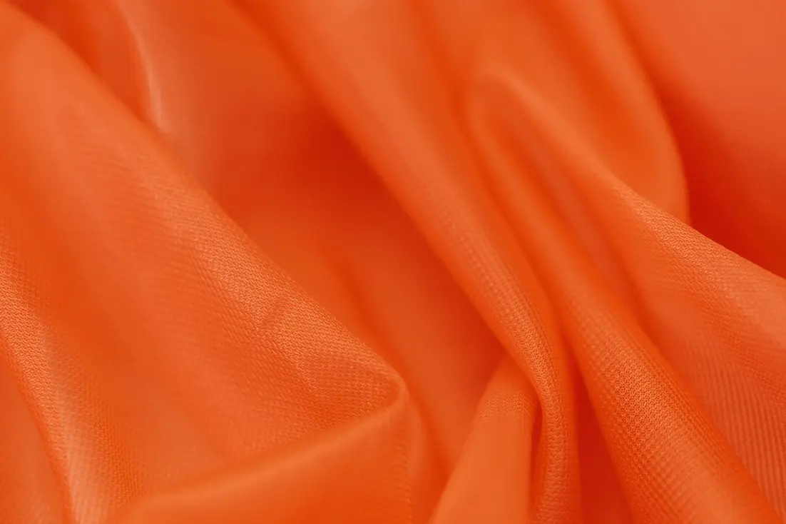 Close-up of a smooth, flowing orange textile fabric with subtle sheen and texture.