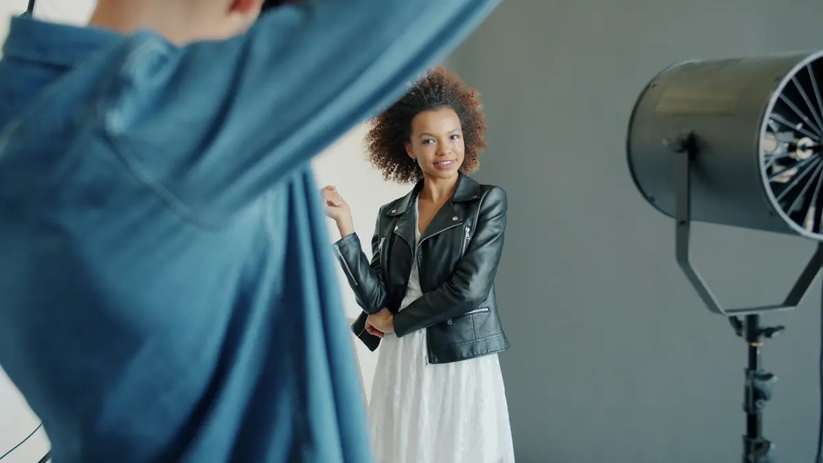 A woman in a leather jacket poses for a photoshoot against a neutral backdrop.