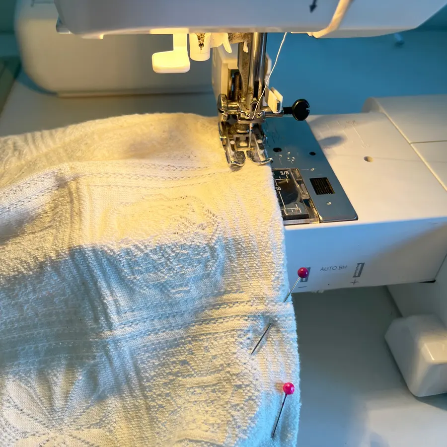 Stretch fabric pinned and being sewn under a presser foot on a sewing machine.